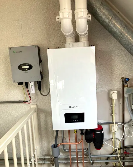 Cv-ketel met afvoerbuizen naast een omvormer aan de wand